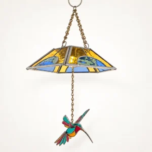 Vista lateral de lámpara colgante con pantalla de vidrio de colores y colibrí suspendido de una cadena.