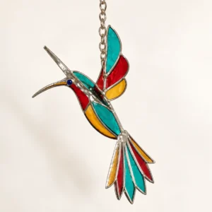 Detalle del colibrí de vidrio con alas extendidas, pico alargado y piezas rojas, verdes y amarillas.